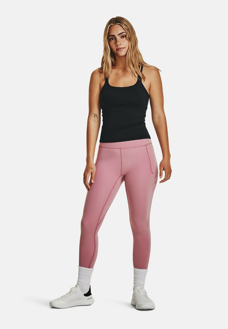 Schwarzes Tanktop und pinkfarbene Leggings mit Nähdetails, getragen mit weißen Turnschuhen und Crew-Socken. Das Model steht aufrecht und schaut nach vorne.