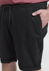 Svarte shorts med elastisk midje og snor. Har side lommer og oppbrett på nederkant. Laget av glatt, lett stoff.