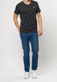 Černé tričko s výstřihem do V vyrobené z bavlny, spárované s modrými džíny. Vykazuje jednoduchý design s malým bílým logem na hrudi.