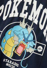 Mornarska majica z velikim grafičnim prikazom Gyaradosa, modrega zmaja podobnega Pokémon-a, z rumenimi poudarki in belim besedilom "POKEMON" ter "#0130."