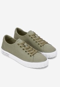 Paire de baskets basses en toile vert olive avec des lacets marron et des semelles épaisses en caoutchouc blanc avec le texte de la marque au talon.
