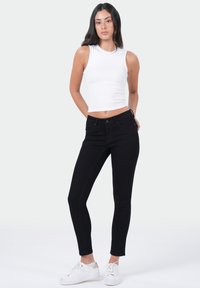 Zwarte skinny jeans met een hoge taille, afgewerkte naden en een licht rekbare stof. Gepaard met een witte mouwloze top en witte sneakers.