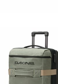Maleta de viaje en tejido verde apagado con un asa superior, un asa retráctil, un bolsillo frontal y un logotipo. Los acentos texturizados realzan el diseño.