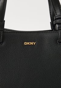 Czarna skórzana torebka o teksturowanej powierzchni, z złotym logo DKNY. Projekt obejmuje dwie czarne rączki oraz szczegółowe przeszycia.
