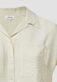 Lichtcrème knoopshirt van een getextureerde stof, met een kraag en twee voorzakken. Eenvoudig ontwerp met een relaxte pasvorm.