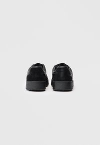 Une paire de baskets noires basses vue de derrière sur un fond blanc uni.