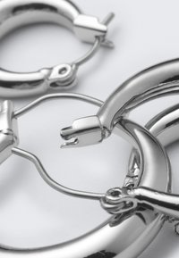 Strieborné kruhové náušnice s lesklým povrchom, vybavené pántovým zapínaním a zakriveným dizajnom, ktoré predvádzajú hladkú textúru a elegantné línie.