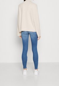 Pull à col roulé crème, oversize, en matière douce, associé à un jean denim bleu ajusté et des baskets blanches. Design simple et moderne.