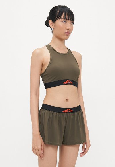 Olive green sports bra with thick black band featuring red logo; paired with matching loose shorts. Smooth, lightweight fabric and streamlined design.