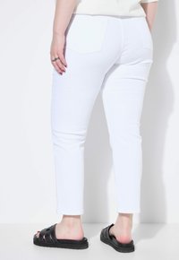 Vita denimbyxor med en slim fit, med två bakfickor och en slät yta. I kombination med svarta slide-sandaler.