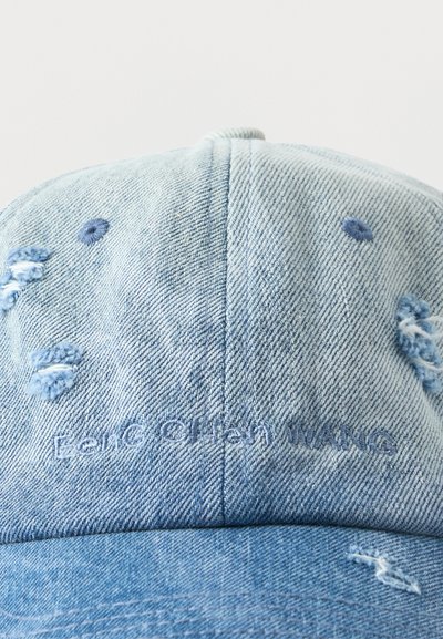 Φωτεινό γαλάζιο καπέλο μπέιζμπολ από τζιν με φθαρμένες λεπτομέρειες και διακριτικό κεντημένο κείμενο "Eero Ohtan WANG" στο μπροστινό πάνελ.