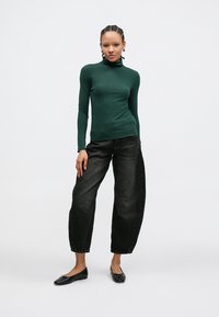 Groen coltrui met lange mouwen gemaakt van stretchstof, gecombineerd met zwarte denim broek in losse pasvorm en zwarte platte schoenen.