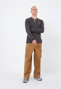 Long-sleeve gray henley shirt with a button placket, paired with tan cargo pants featuring side pockets, and gray athletic shoes.