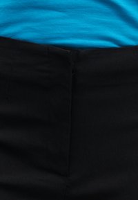 Μπλε ύφασμα που έχει μπει μέσα σε μαύρο παντελόνι με ψηλή μέση, με ορατό κεντρικό φερμουάρ στο παντελόνι.