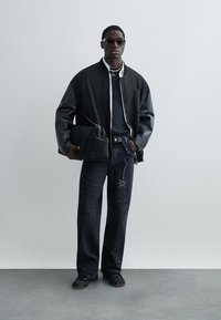 Fekete bombázó dzseki kontrasztos bőr ujjakkal, fekete póló, szegecses, kopott sötét farmer, fekete cipő és strukturált fekete táska.