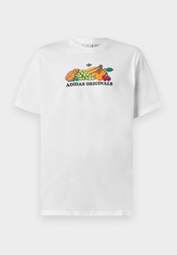 T-shirt bianca in cotone con una grafica colorata di frutta e il testo "ADIDAS ORIGINALS" in grassetto nero. Maniche corte, colletto tondo.
