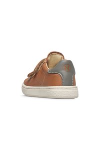 Sneaker in pelle marrone con linguetta grigia, suola in gomma bianca e cinturino in Velcro, visto da dietro su uno sfondo bianco.