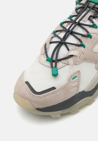Lightweight sneaker featuring a mix of materials: suede in tan, mesh in white, grey accents, and green lacing details. Thick rubber sole.