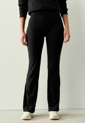 Schwarze, weit ausgestellte Hosen aus einem weichen, dehnbaren Stoff. Sie verfügen über einen breiten Bund mit raffiniertem Detail und eine elegante Passform über die Beine.