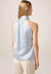 Top halter azzurro chiaro in satin, con un motivo a diamante grigio. Collo arricciato e texture liscia con una vestibilità comoda.