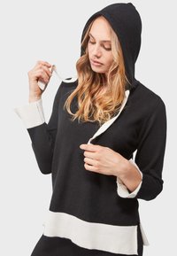 Sudadera negra con capucha, con acentos en blanco en los puños y en el dobladillo. Cuenta con un cordón y un corte relajado con una textura suave.