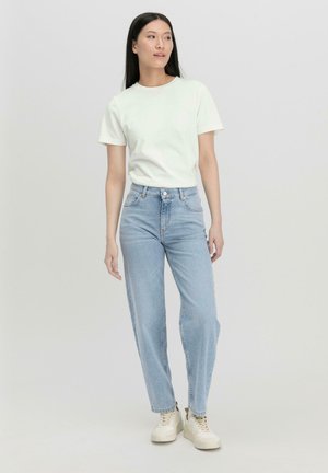 Witte katoenen t-shirt gecombineerd met hooggerande lichtblauwe jeans. Model draagt beige sneakers. Minimalistisch ontwerp met een aansluitende snit.