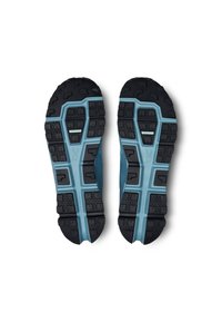 Paire de semelles de chaussures de course bleues et noires avec des crampons profonds et des motifs géométriques sur fond blanc.