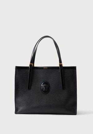 Sac cabas en cuir noir avec poignées doubles, accents dorés et un emblème Méduse en relief au centre avant.