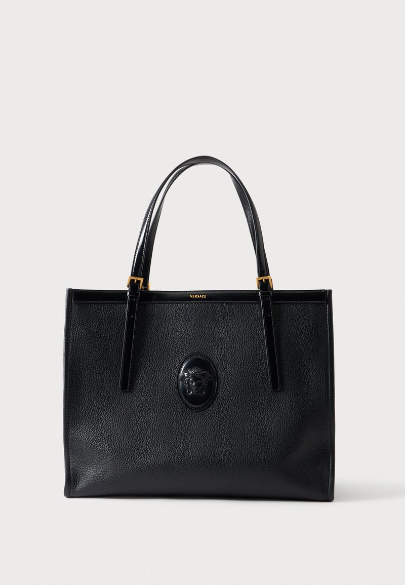 Sac cabas en cuir noir avec poignées doubles, accents dorés et un emblème Méduse en relief au centre avant.