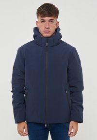 Veste isolante bleu marine avec un col haut, fermeture éclair sur le devant et deux poches latérales. Texture lisse et capuche pour une protection supplémentaire.
