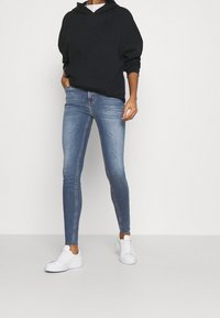 Sudadera con capucha negra y vaqueros ajustados de mezclilla azul claro, combinados con zapatillas blancas, mostrando un atuendo casual con un ajuste relajado y mínimos detalles.