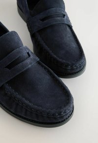 Paire de mocassins en daim bleu foncé avec couture mocassin et une bride horizontale sur le dessus.