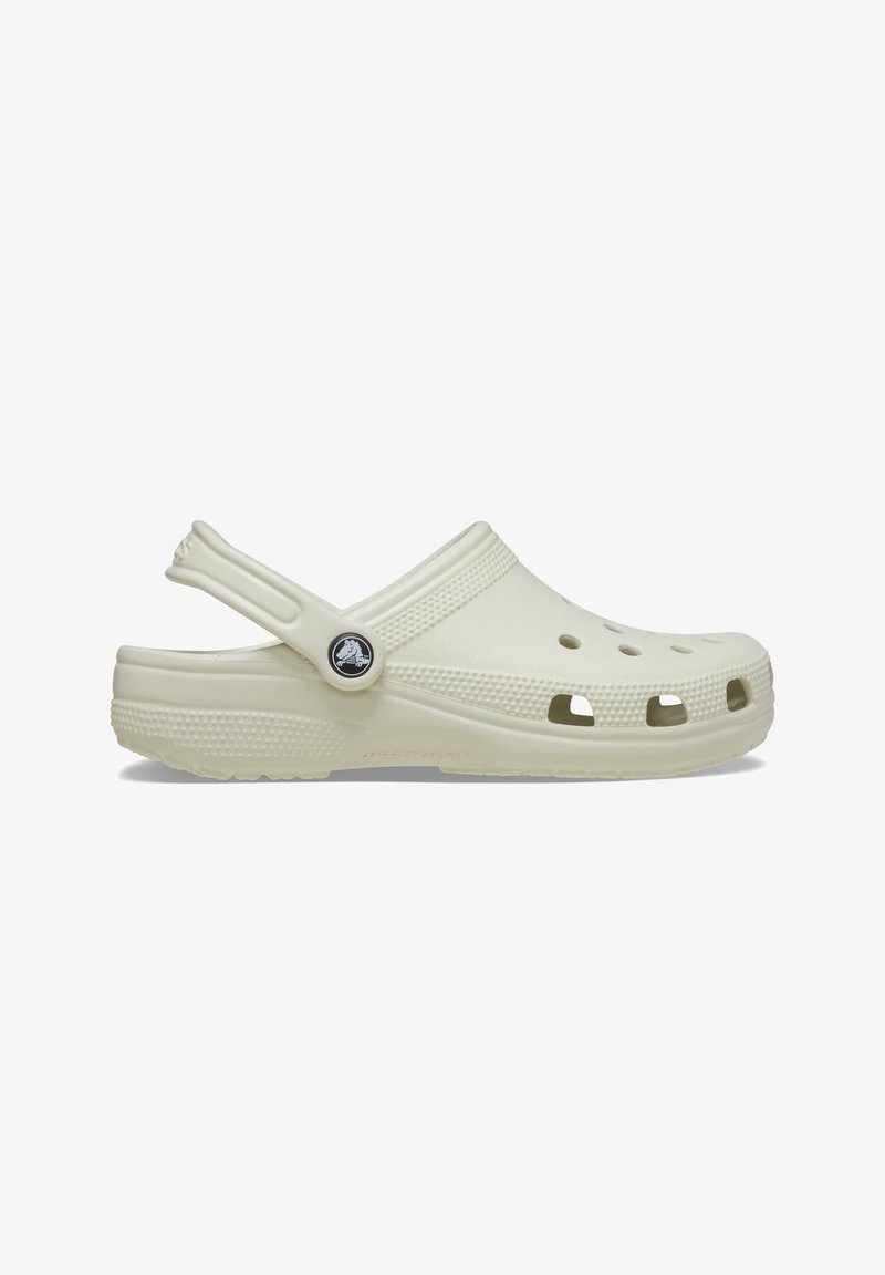 Sabot en caoutchouc blanc cassé avec des trous de ventilation, semelle texturée et bride de talon réglable avec un logo circulaire noir.