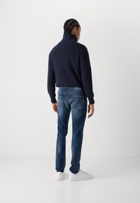 Marine striktrøje, afslappet pasform, høj krave; blå denimjeans, slim fit, let slidte; hvide sneakers, minimalistisk design.