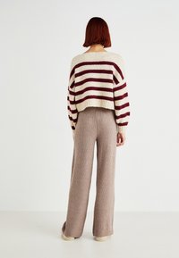 Gehaakte gestreepte trui in crème en bordeaux, gecombineerd met breede ribbelachtige beige broeken. Zachte textuur en ontspannen ontwerp.