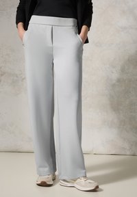 Pantalons larges gris clair avec une texture lisse, un devant plissé et une taille élastique, associés à des baskets beiges.