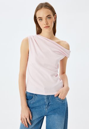 Top rosa chiaro, off-shoulder in tessuto morbido con dettaglio drappeggiato. Indossato con jeans in denim blu a vita alta. Design semplice e aderente.