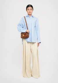 Blue and white striped oversized shirt, beige wide-leg trousers, and a small brown shoulder bag with a gold clasp. Simple, relaxed design.