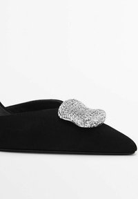 Svarta mocka ballerinaskor med spetsig tå, prydda med en silverfärgad rhinestones accent på ovandelen. Slät yta, elegant design.