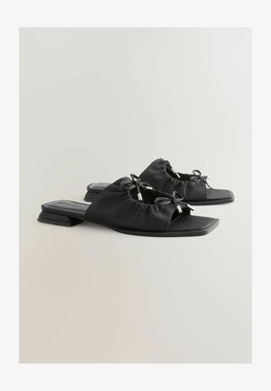 Black slide-on shoes featuring a textured fabric upper with gathered detailing and a silver accent. Square toe and low block heel design.