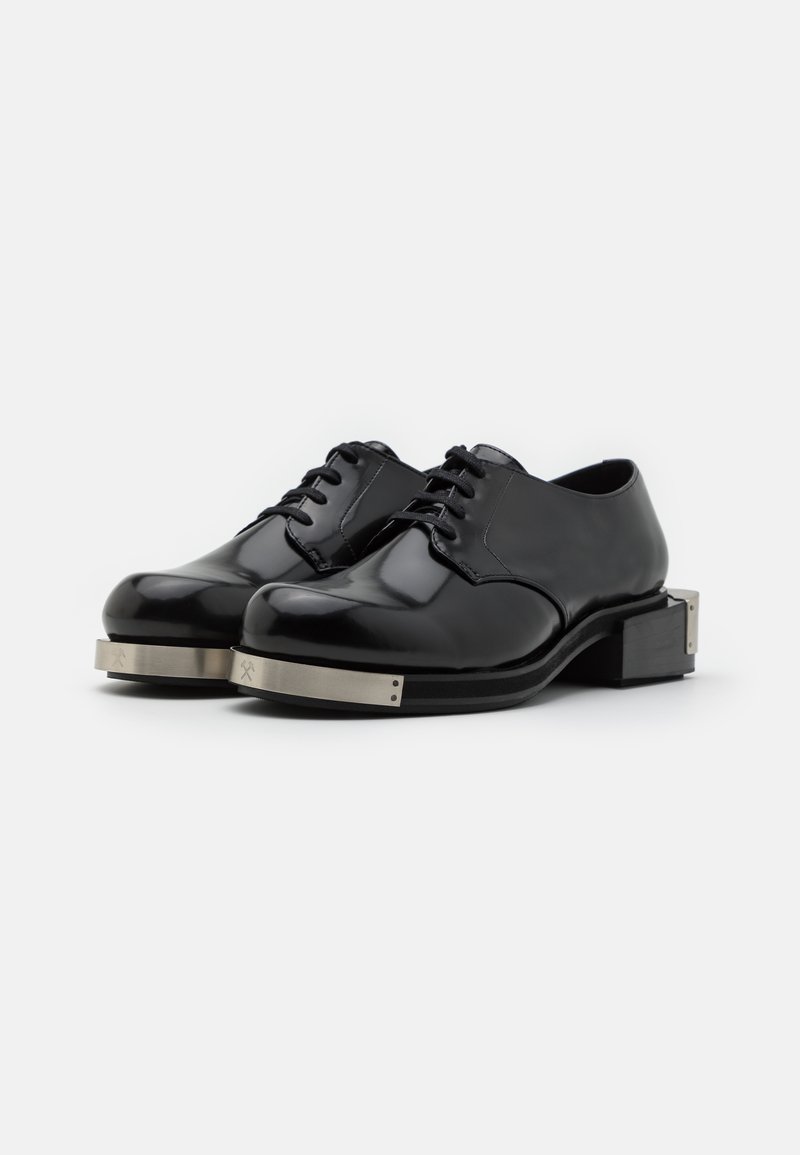Scarpe in pelli nere lucide con punta arrotondata, design con lacci e dettagli metallici argento sulla suola. Cuciture dettagliate visibili.