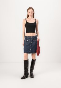 Denim skjørt med frontknapper, to lommer og en tettsittende design. Kombinert med en svart kort tanktop og lårhøye, glansfulle svarte støvler.