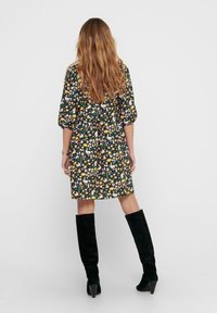 Vestido floral con fondo negro, que presenta mangas cortas abullonadas, una cintura fruncida y un dobladillo a la altura de la rodilla. Combinado con botas altas negras.