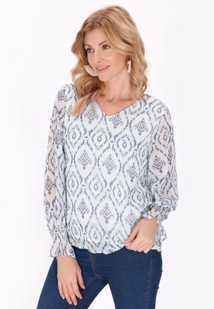 Blusa azzurra a fantasia con scollatura a V, dotata di maniche lunghe e polsini arricciati. Realizzata in tessuto trasparente con motivo ikat.