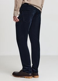 Dunkelblaue Cordhose mit schmaler Passform, ausgestattet mit zwei Gesäßtaschen und einer glatten Textur, kombiniert mit braunen Schnürschuhen.