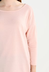 Hellrosa, langärmliges Oberteil mit einem Bootsausschnitt und weichem Stoff, mit lockerer Passform und dezentem Strickmuster.