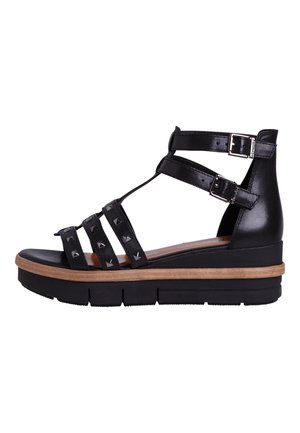 Sort kile-sandal med tre nittebesatte remme, to justerbare ankelspænder og en tyk brun og sort sål.