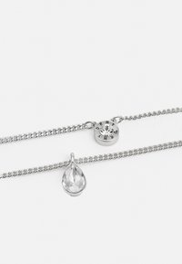 Silver-tone chain necklace with a round charm featuring a clear stone and a pear-shaped pendant. The chain is textured and linked.