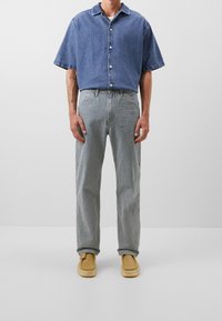 Camisa vaquera azul de manga corta, abotonada, con pantalones a rayas grises y blancos, combinada con zapatos tipo slip-on color tostado. Diseño sencillo y relajado.