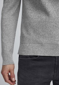 Pull en tricot gris texturé avec manches longues et ourlet côtelé, associé à un jean en denim foncé. Mettez l'accent sur le motif tissé et la couleur du tissu.